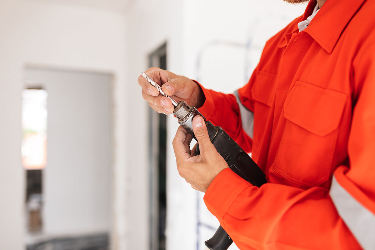 Close up builder in orange work clothes holding drill machine in